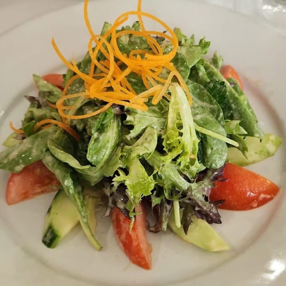 Fresh Italian salad with mixed greens, tomatoes, cucumbers, and shredded carrots on a white plate.