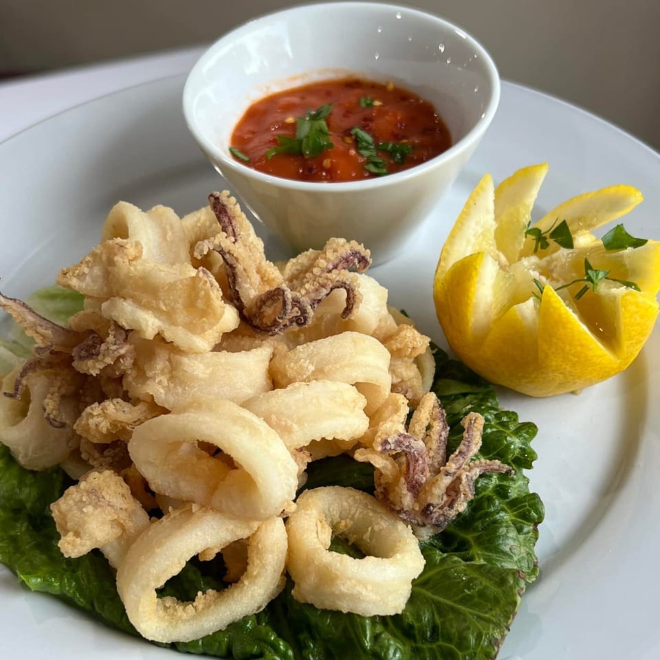 Crispy fried calamari with marinara sauce and a lemon wedge on a white plate.