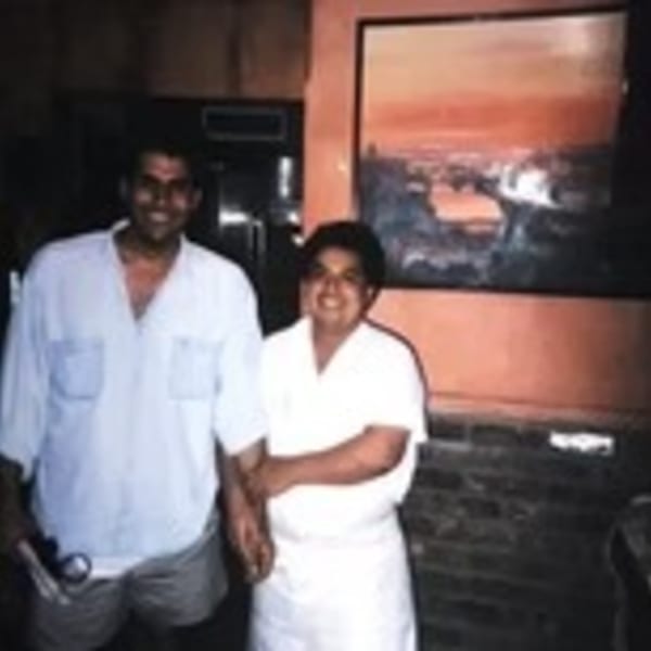 Two smiling men, one in a light shirt and shorts, the other in a white chef's coat.