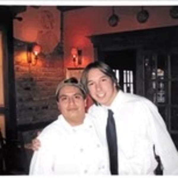 Two smiling men, one in a chef's coat and one in a white shirt and tie, pose in an Italian restaurant.
