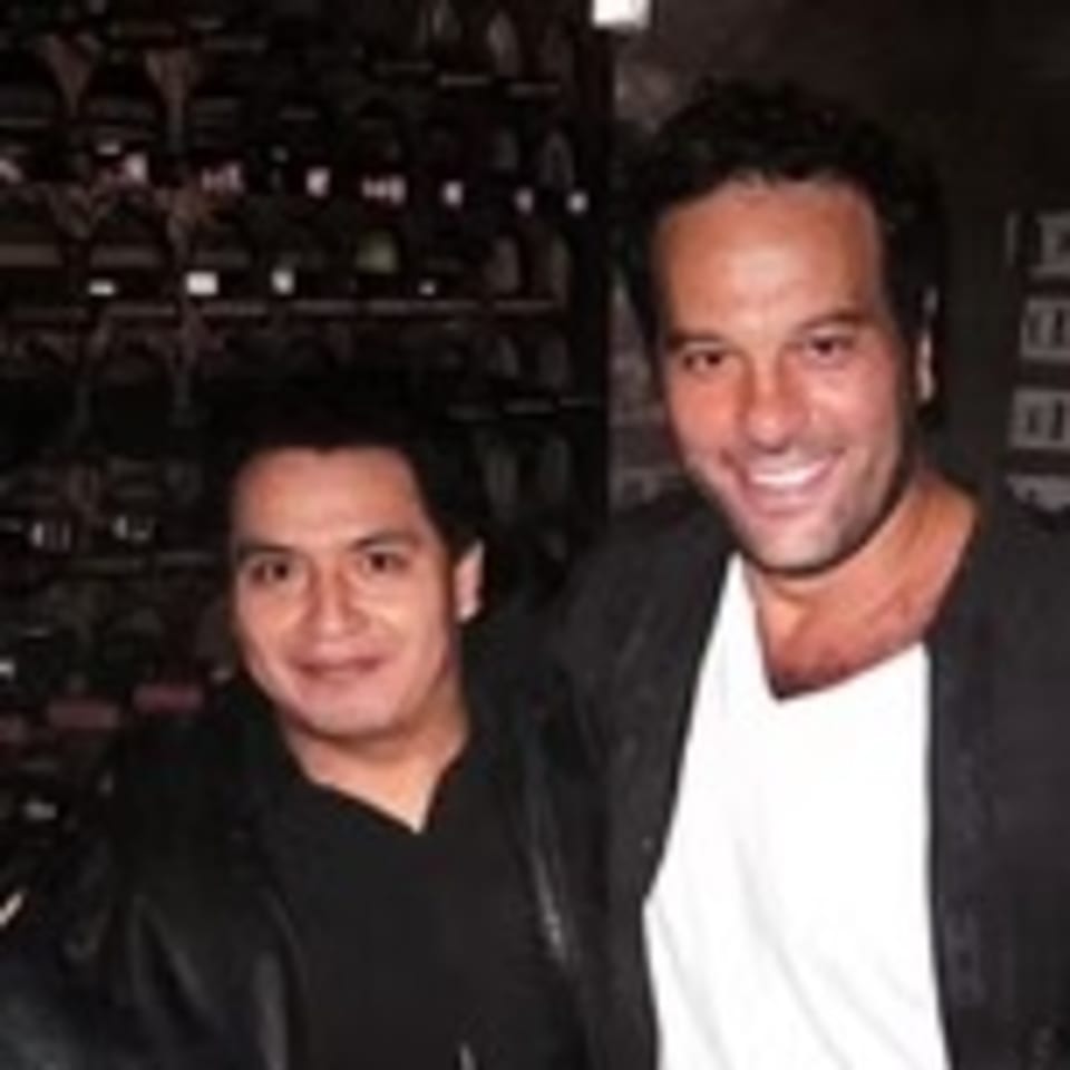 Two men smiling at the camera, one in a black jacket and the other in a white shirt and black jacket.