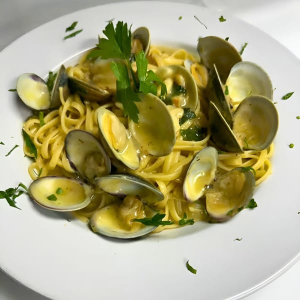 Linguine pasta with clams in a white wine sauce, garnished with fresh parsley on a white plate.