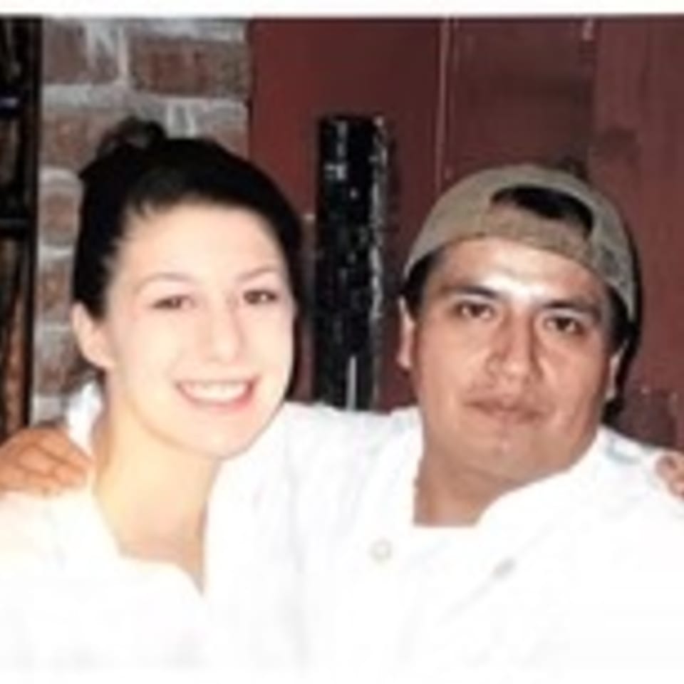 Smiling woman and man in a baseball cap, both in white shirts, posing together.