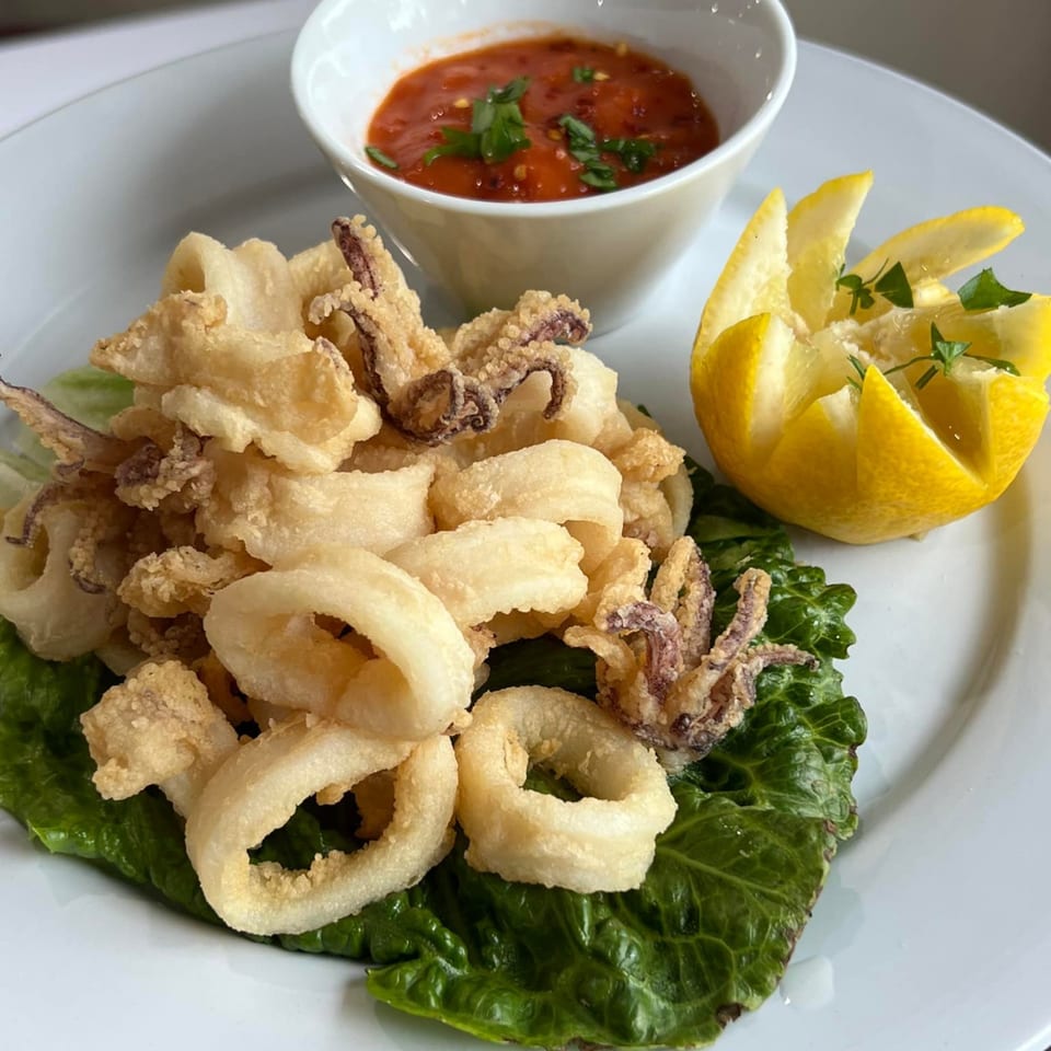 Crispy fried calamari with marinara sauce and a lemon wedge on a white plate.